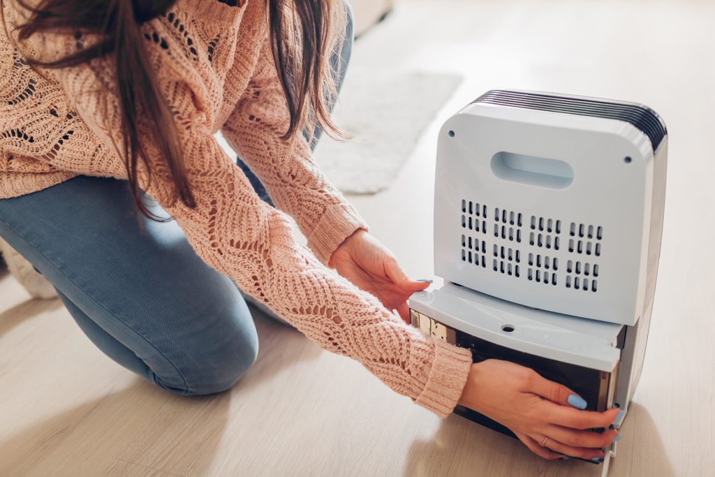 a homeowner wearing a pink jumper and jeans emptying a dehumidifier in order to prevent mould on the walls